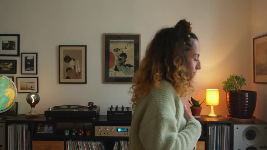 A woman is standing in her living room dancing in front of her turntable and record collection