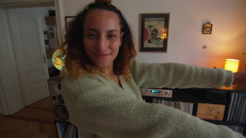 Woman smiles while dancing in room with shelves full of records and cds