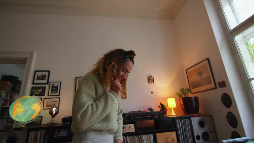 A woman is standing in her living room dancing in front of her turntable and record collection