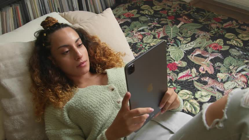 A woman is laying down and browsing on a tablet