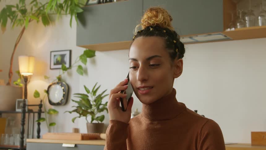 A young woman speaks on a smartphone while sitting indoors during the day
