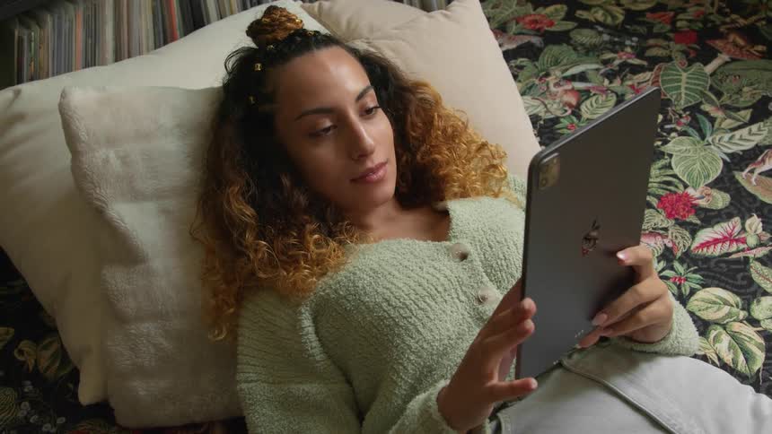 A woman scrolls through her tablet while lying on the ground