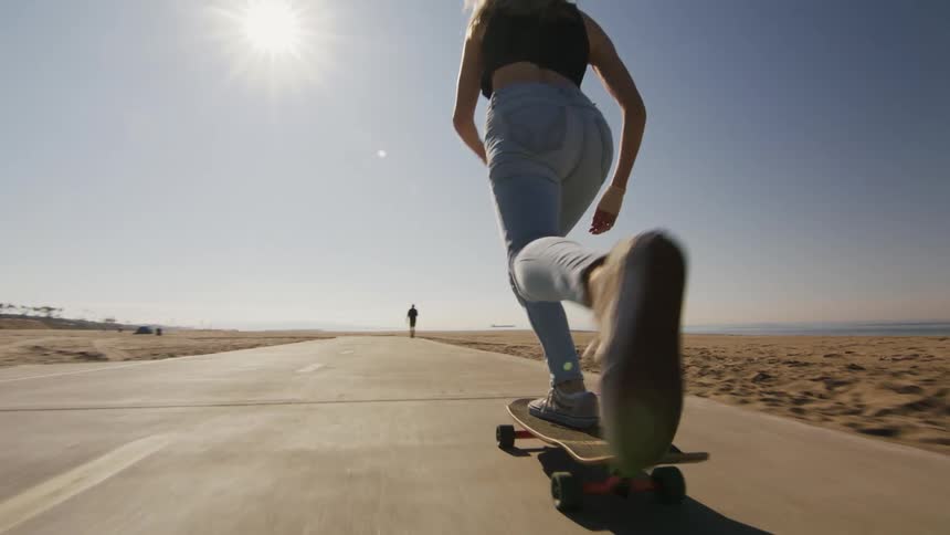 A woman rides her skateboard down a trail on the beach