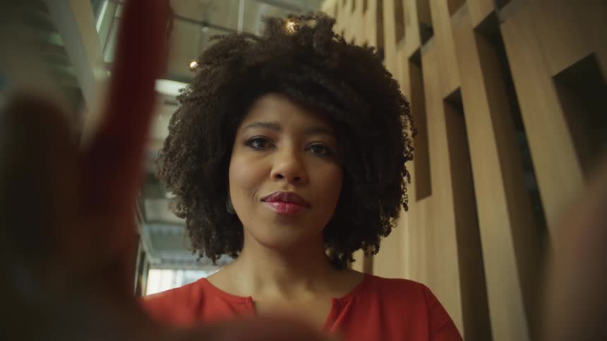 A woman is walking down a hallway and making movements and gestures with her fingers