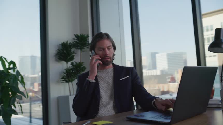 Man working in office with view of city answers call on smartphone
