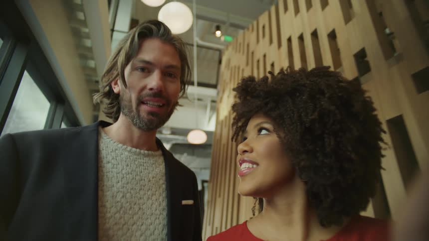 Woman with curly hair and red blouse shows stuff on tablet walking corridor in the office