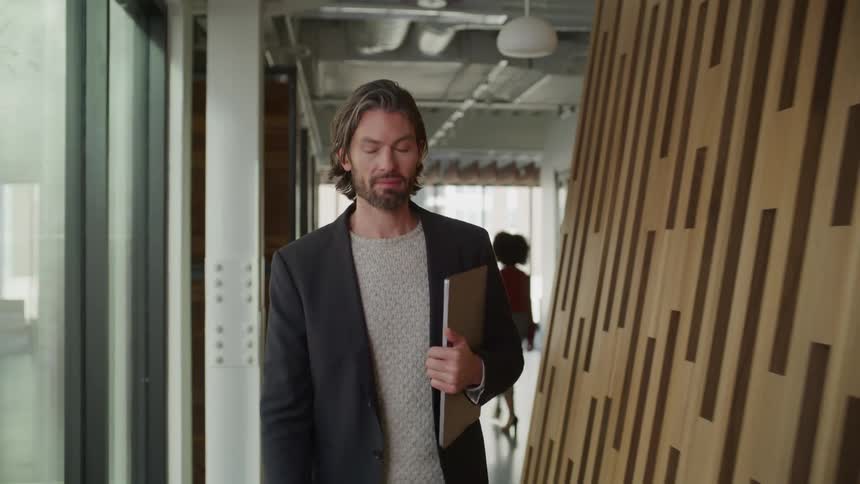 Man walks along hallway holding laptop as fellow employee walks the opposite way