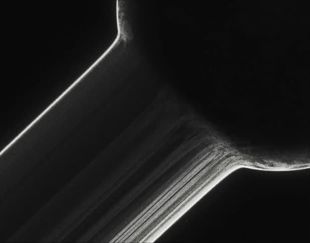 Small powder particles flow through white lines moving across a dark surface