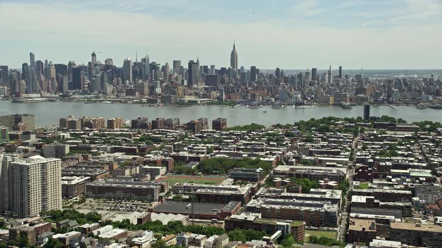 Aerial footage of Midtown Manhattan skyline and Jersey City urban neighborhoods in New Jersey and New York with an approaching and sunny day time showcasing the high rise towers and buildings in the urban residences