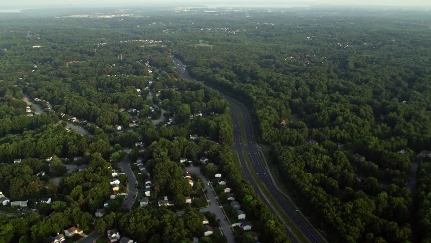 An aerial footage capturing the suburban neighborhoods in Burke Virginia during sunset showing the residential houses transportation on highways and the hazy ambiance of the region