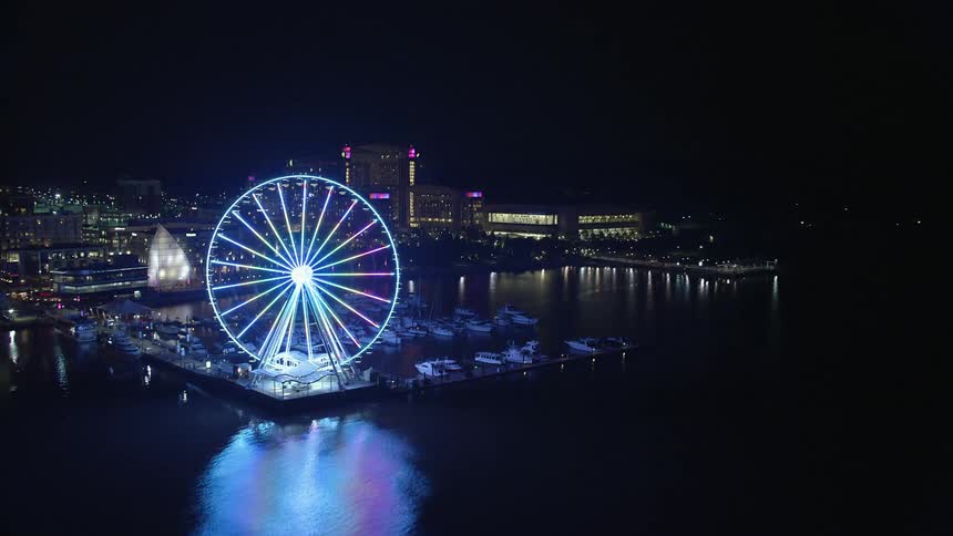An aerial shot of the lit-up Capitol Wheel and marina with Gaylord National Resort and Convention Center visible in the background