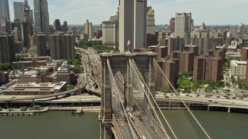 A stunning aerial footage showcasing the iconic Brooklyn Bridge and Lower Manhattan skyline capturing the hustle and bustle of cars and transportation on sunny New York City day