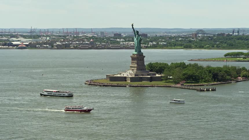 Stunning aerial footage of Statue of Liberty and ferries passing by in New York Harbor during daytime