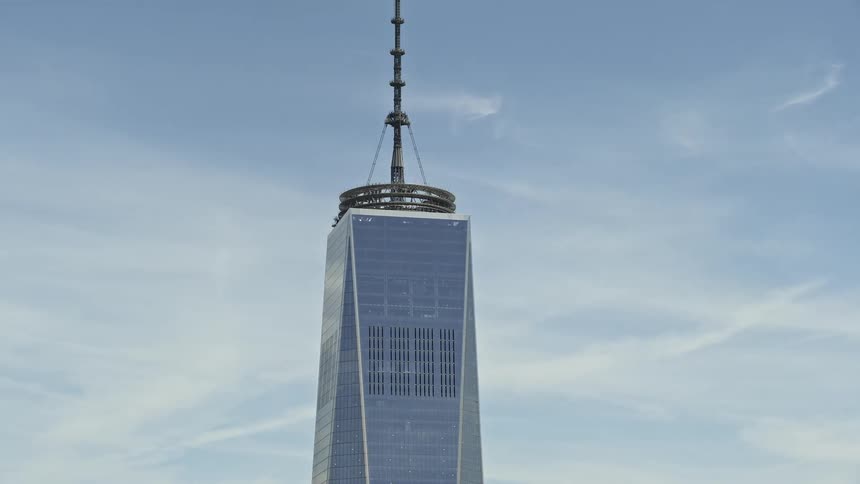 Aerial footage of One World Trade Centers top with partly cloudy skies over Lower Manhattan New York City during the daytime