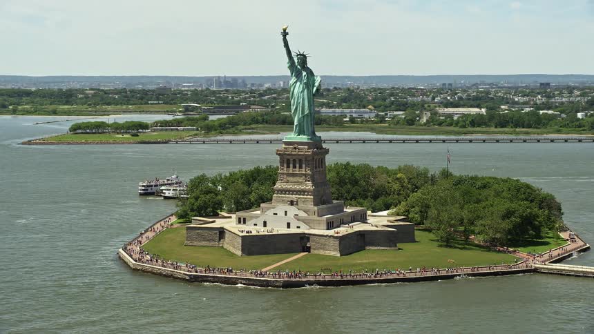 Aerial footage of tourists enjoying the sunny day while flying past the Statue of Liberty in New York Harbor