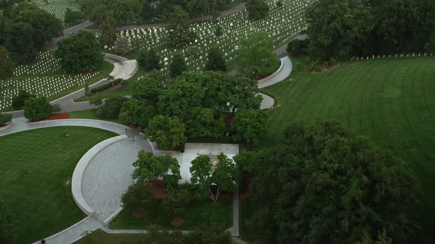 Aerial footage flying over trees at Arlington National Cemetery reveals President John F Kennedy Gravesite during twilight in Virginia