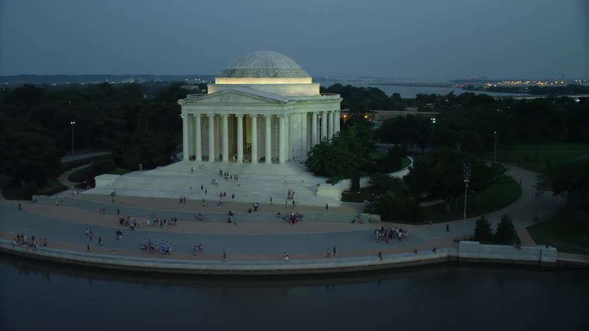 Aerial footage of the Jefferson Memorial at night surrounded by tourists on the steps in Washington DCs historic district during twilight