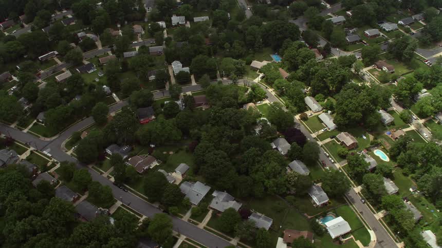 An aerial view from above tilting down to show suburban homes trees and swimming pools in Springfield Virginia on a partly cloudy day