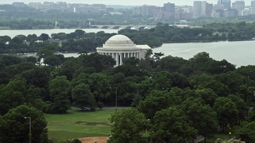 Aerial footage of the Jefferson Memorial partially hidden by trees in West Potomac Park Washington DC on a hazy day showing an iconic structure of historical significance