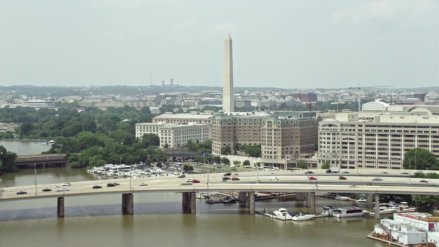 Aerial approach to the bridge government buildings and Washington Monument in Washington DC with a view of the river boats and cars crossing the bridge during the daytime