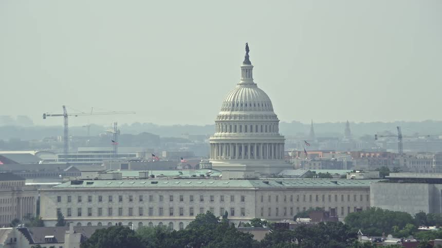 Hazy aerial shot of United States Capitol dome towering over office building rooftops in Washington DC on a summer day