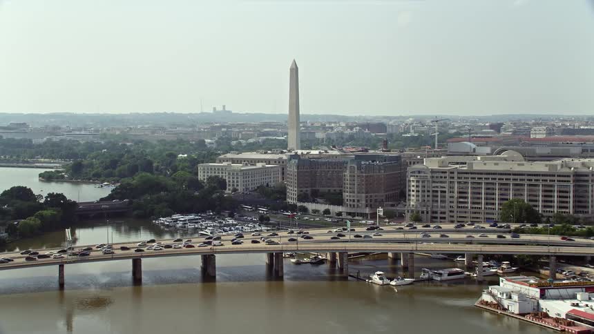 Aerial view of heavy traffic approaching a bridge with office buildings and the Washington Monument in Washington DC during daytime