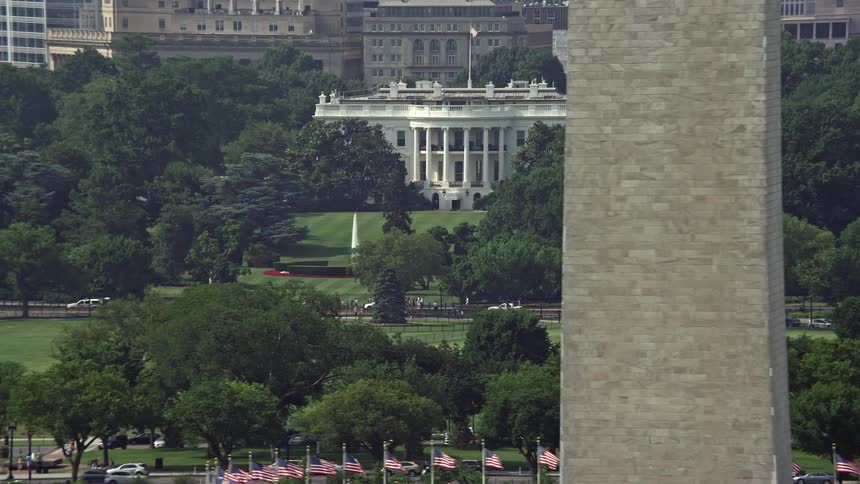 Aerial footage of the White House and South Lawn in Washington DC during daytime with a reveal of part of the Washington Monument showcasing the iconic government building and historical landmark