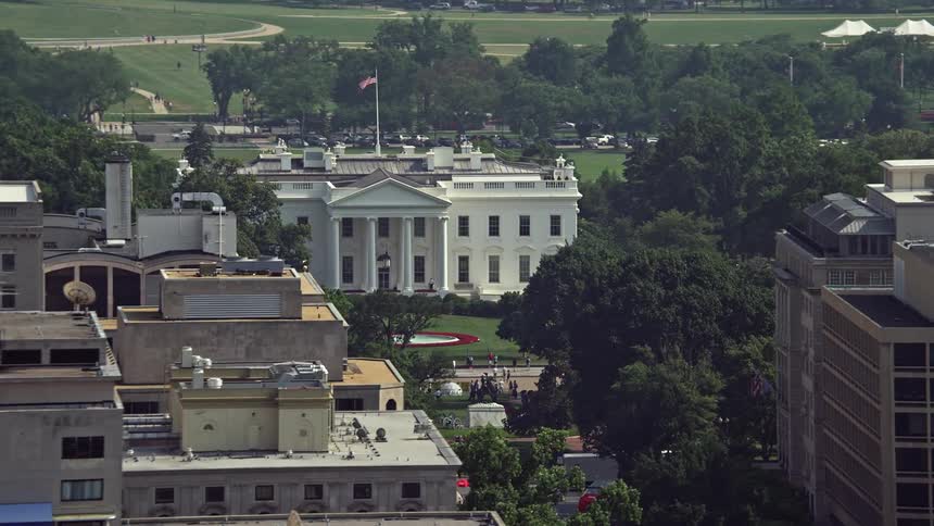 Aerial footage of the White House being revealed over office building rooftops with the Washington Monument in the background