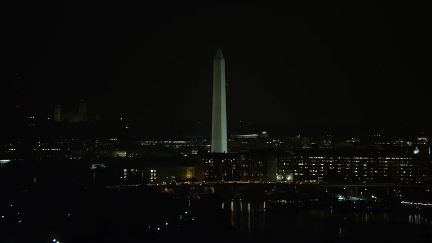 Washington Monument illuminated at night behind office buildings in DC