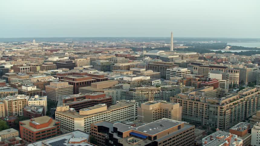 Watch the iconic Washington Monument standing tall over the hazy city skyline during a beautiful sunset from an aerial view