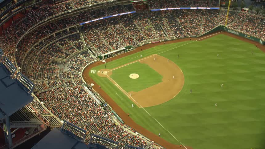 Aerial footage captures a baseball game at the Nationals Park in Washington DC during twilight with players and spectators seen in the stadium below