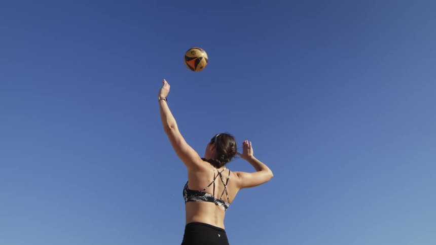 A woman serves a volleyball outdoors during the day