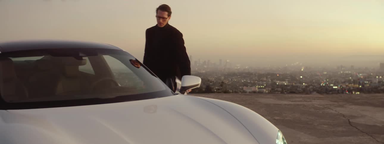A man standing on the edge of a cliff near his car walks over to the car and gets in