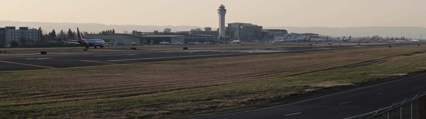 Automobiles travel on roads near an airport as an airplane moves on the runway