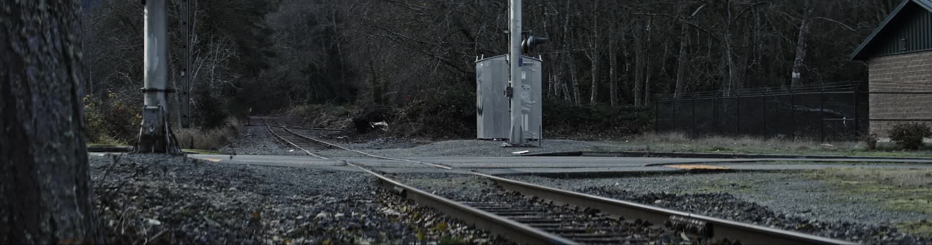 Bare train tracks with a road going over them and a car traveling over the road
