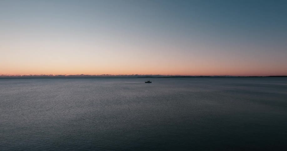 Camera soars over a lone fishing boat on the ocean at sunrise
