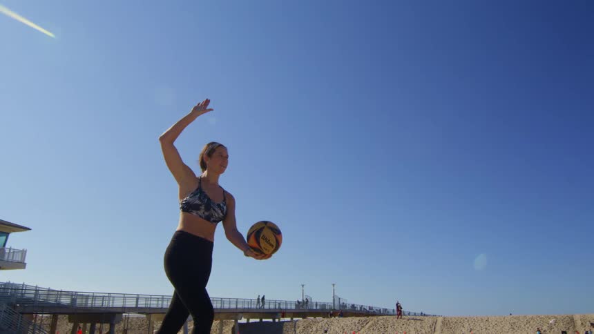 A woman serving a volleyball on a sandy beach
