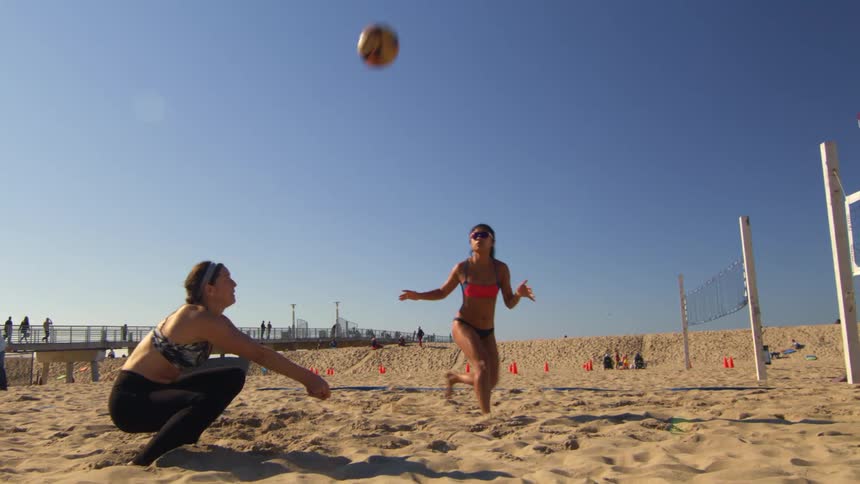 Two women passing a volleyball to each other on a sandy court