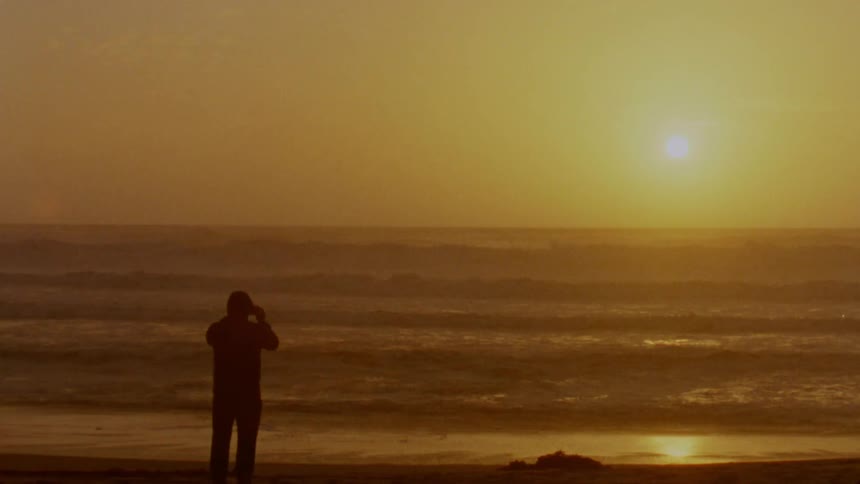 Silhouette of a man standing on a beach in front of the ocean at sunset