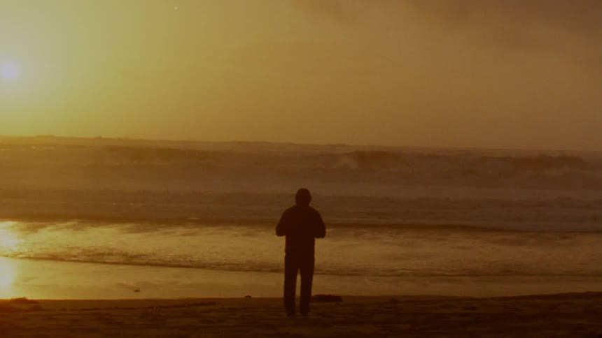 A silhouette of a person taking a picture of the sunlit ocean