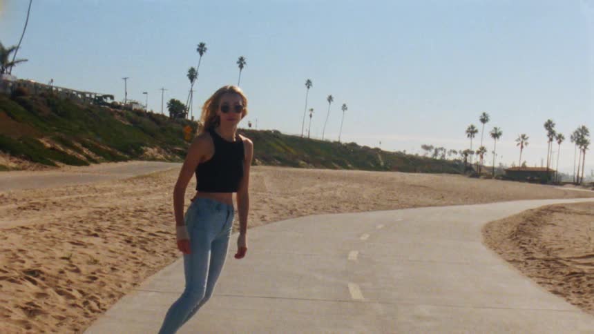 A woman skateboarding down a sidewalk wearing a black shirt and sunglasses