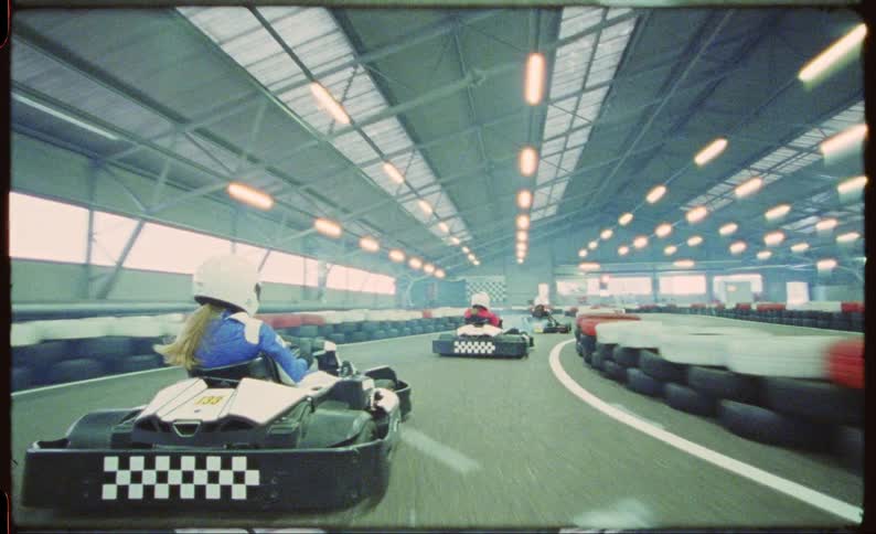 A group of children race on go karts in a warehouse