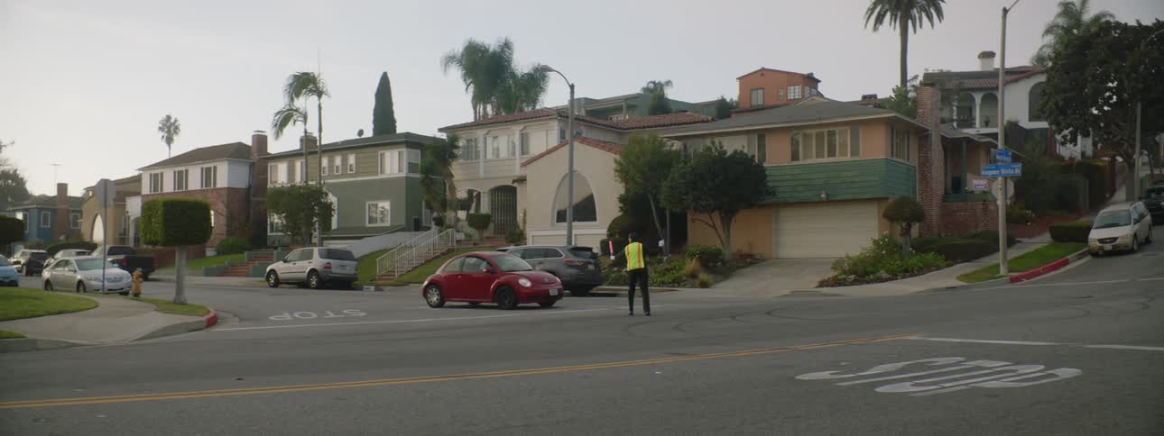 A red car drives past a crossing guard despite him being told to stop because the guard is waving traffic across that does not exist
