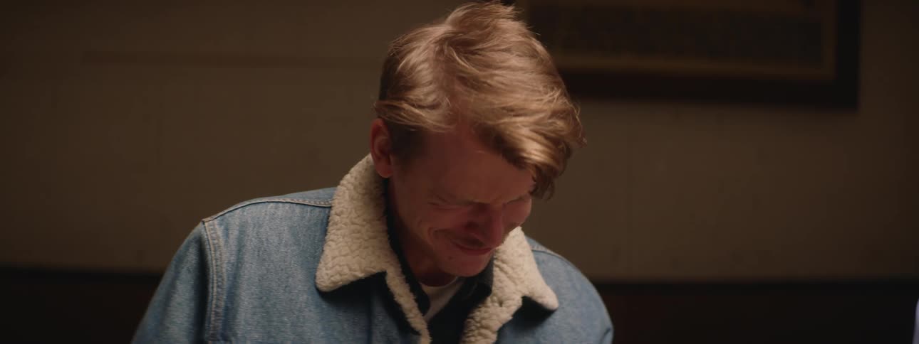 Man with a mustache wearing a denim jacket talks and looks distressed