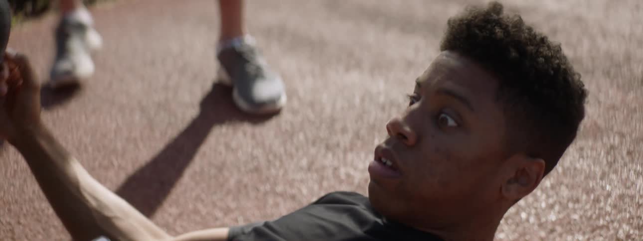 A teenage male runner lies passed out on the ground and his teammates help wake him up