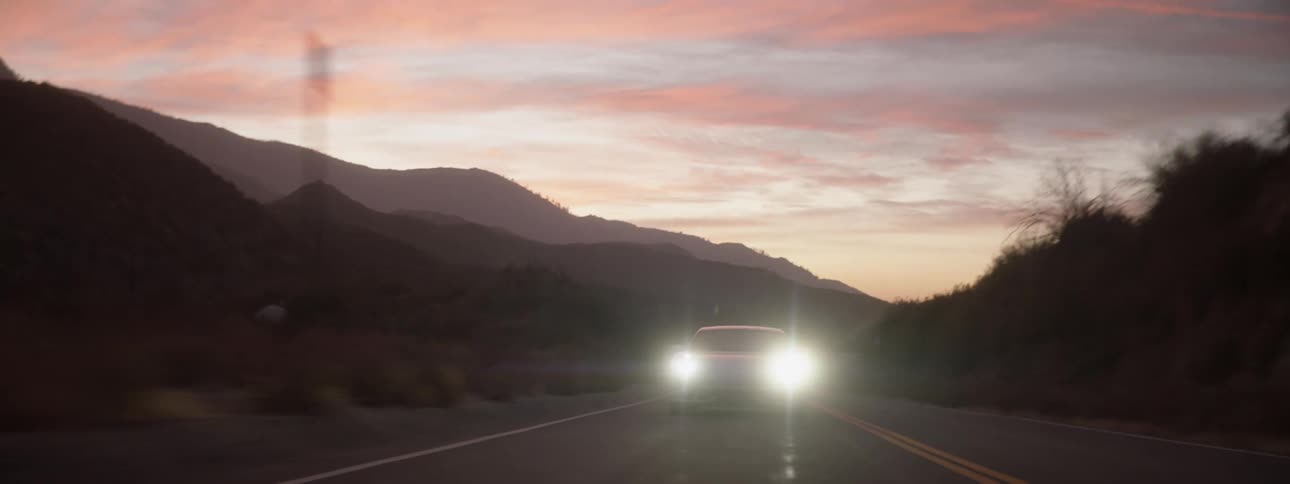 A white cars headlights shining forward with a mountain view in the background
