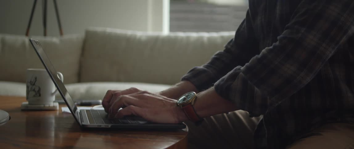 A man is sitting indoors and typing on a laptop