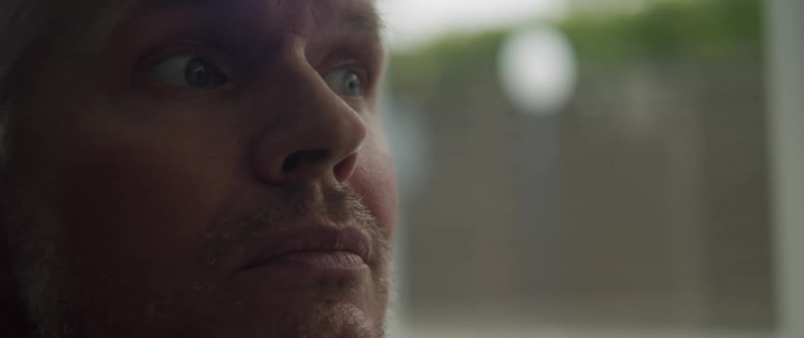 A man is in a room near a window as he looks around and smiles