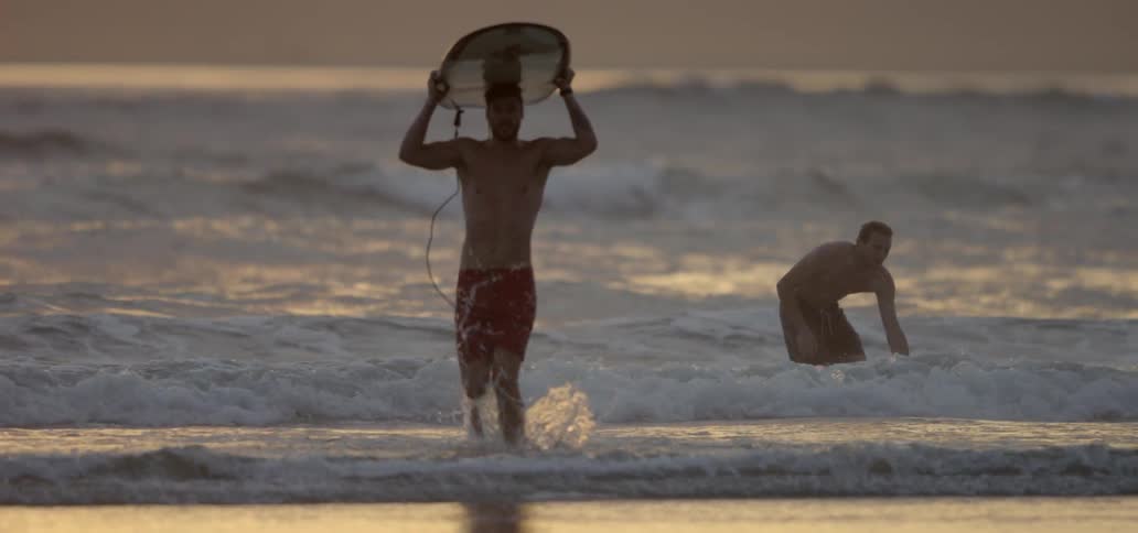 Two people with surfboards walk out of the water