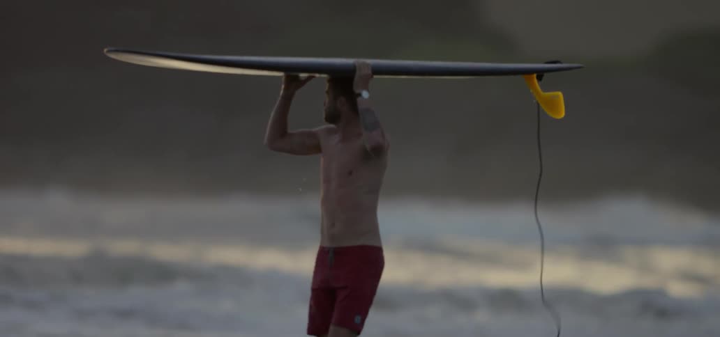A man is walking with a surfboard on his head